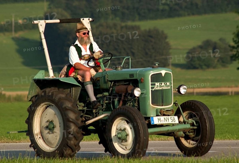 Traditionally dressed farmer in lederhosen and Tyrolean hat on a tractor, Dietramszell, Bavaria, Germany, vintage, retro, Europe