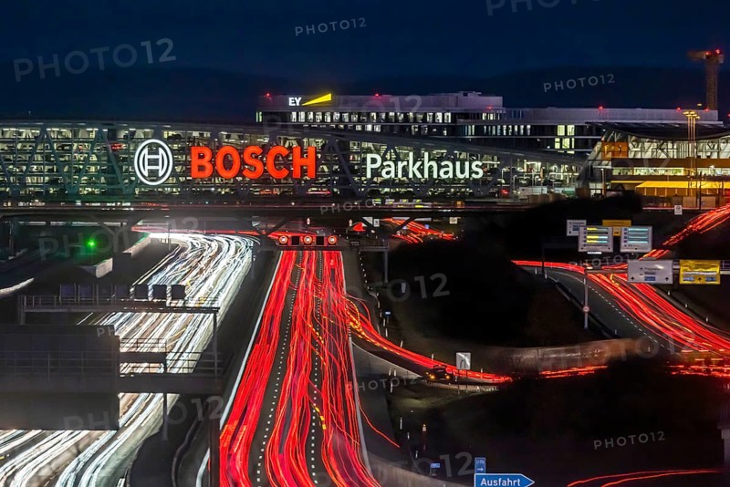 A8 motorway at Stuttgart Airport with Bosch multi-storey car park in the evening, cars create light trails. The 440 metre long construction offers space for 4200 vehicles. Bosch owns the naming rights, the stylised ignition anchor measures 12 metres in diameter. This makes it one of the largest neon signs in the world. Stuttgart, Baden-Wuerttemberg, Germany, Europe