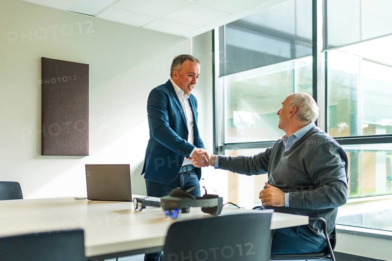 Business people shaking hands in the office next to futuristic goggles