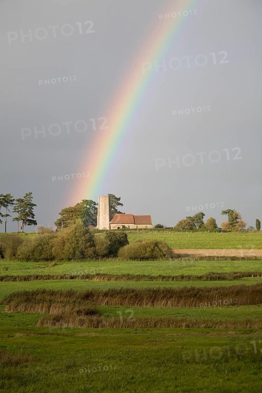 The end of a rainbow lights up the tower of All Saints church, Ramsholt, Suffolk, England, United Kingdom, Europe