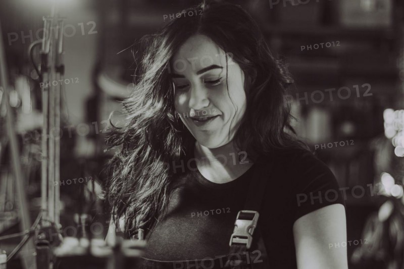 Hispanic latino long haired brunette sexy woman mechanic examining a car part in a well-equipped workshop, a complete tool panel in the out of focus background with bokeh effect