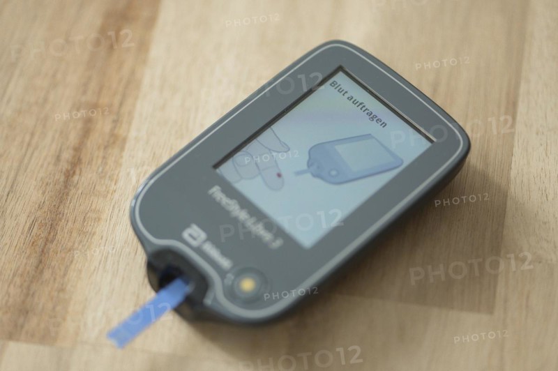 Blood glucose meter with test strips lying diagonally in the centre on a wooden table, ready for a blood glucose measurement, diabetes treatment, glucose measurement, Ruhr area, Germany, Europe