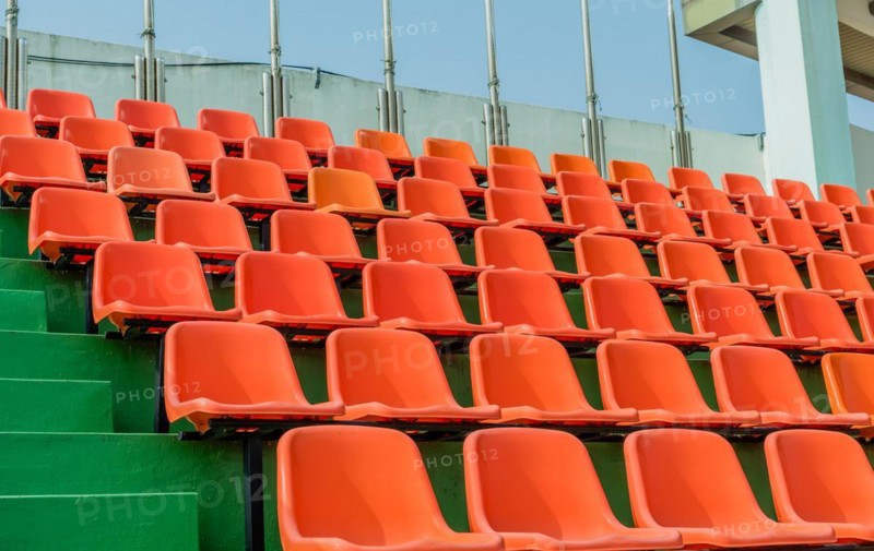Rows of empty orange seats ascending green steps at a stadium, in South Korea