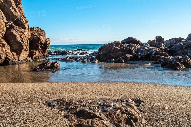 Sandy beach with large rocks and waves crashing in from the sea under a blue sky, in South Korea