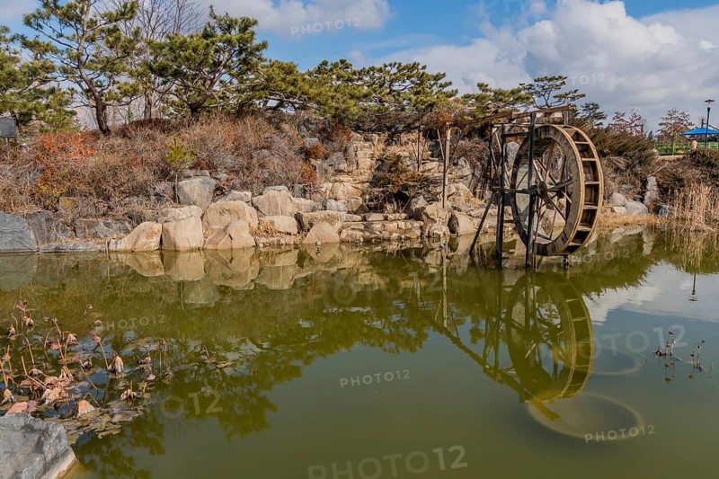 A water wheel beside a peaceful pond with rock formations and clear reflections, in South Korea
