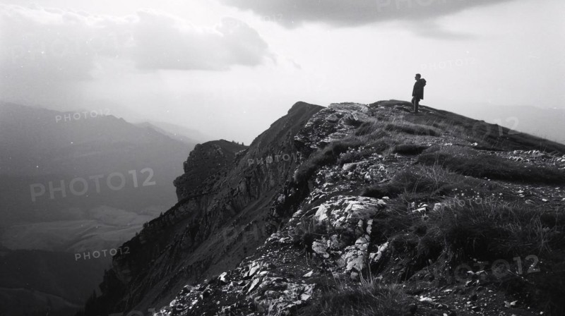 A hiker stands on a mountain peak surveying the surrounding rugged terrain, AI generated