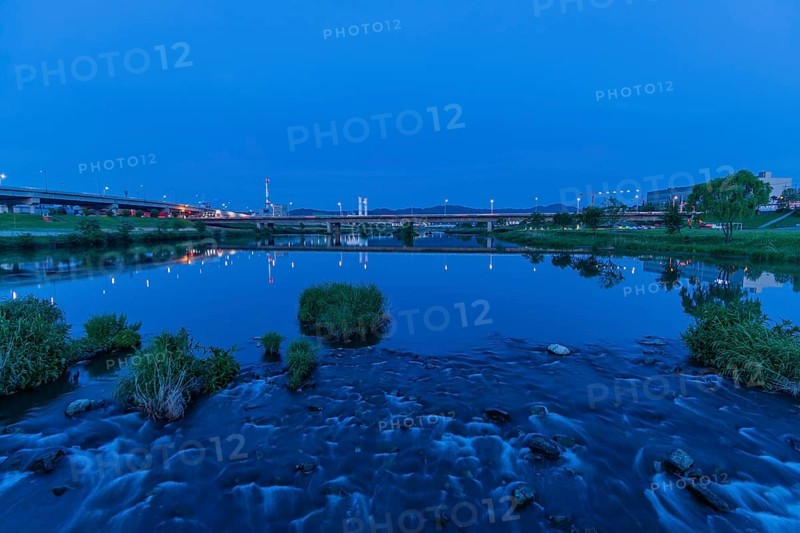 Pebbled riverfront reflecting bridge lights at twilight, in South Korea