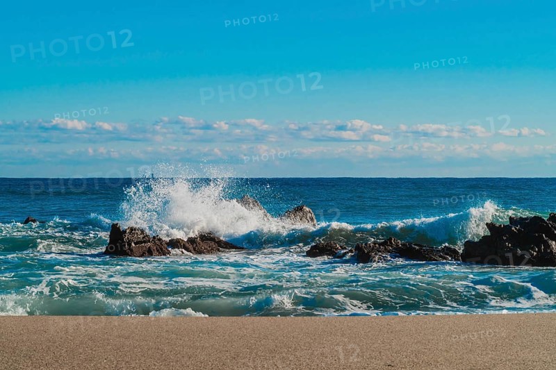 Spray rises as waves collide with rocky outcrops on a sandy beach, in South Korea