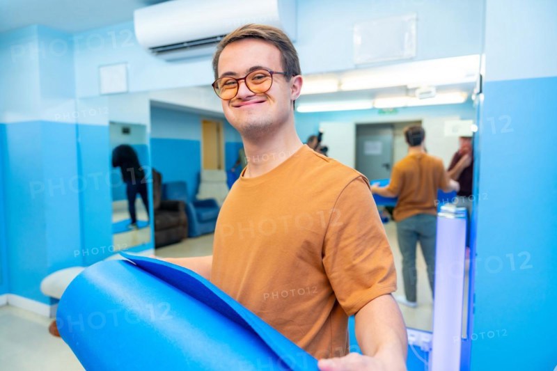 Happy and satisfied man with down syndrome after yoga class holing a mat
