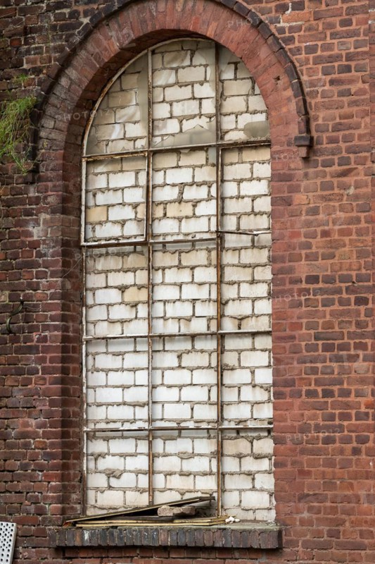 Arched brick window that has been bricked up and shows patina