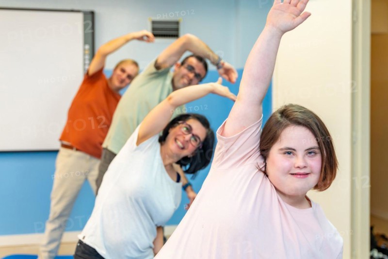 Focus on a woman with down syndrome and a group of people with special needs stretching in the gym