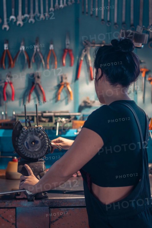 Female hispanic Mechanic working at a bench in a well-equipped workshop from behind, a complete tool panel in background with bokeh effect, traditional male jobs by Mixed-race latino woman