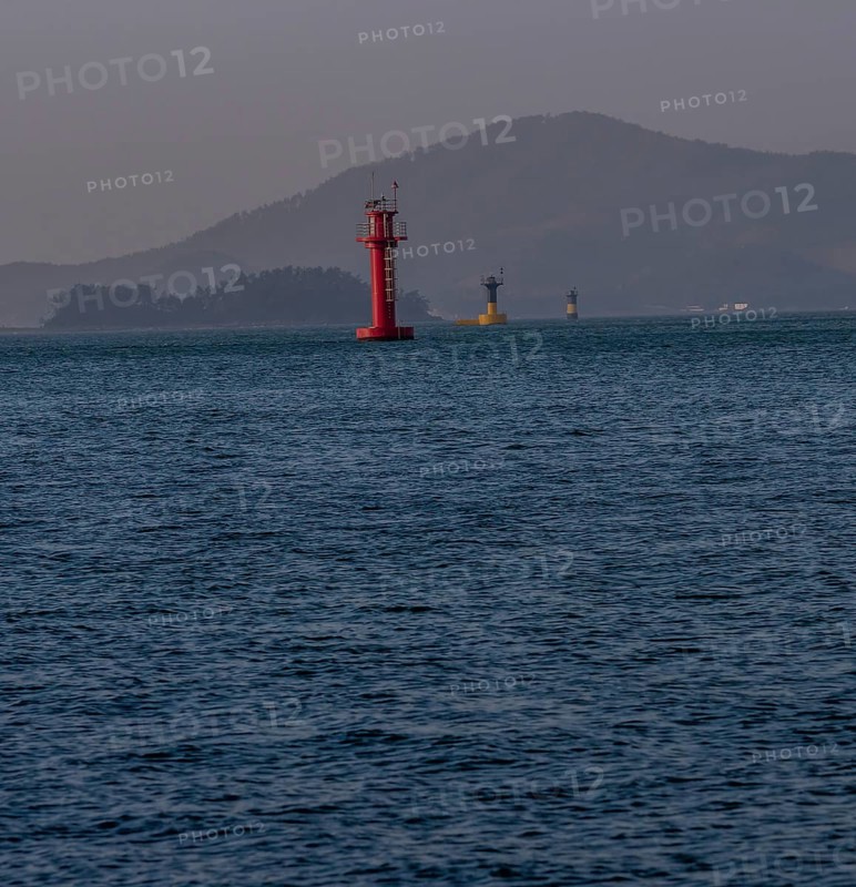 Three small lighthouses in a harbor with small mountains shrouded in fog and mist in the background in Namhae South Korea