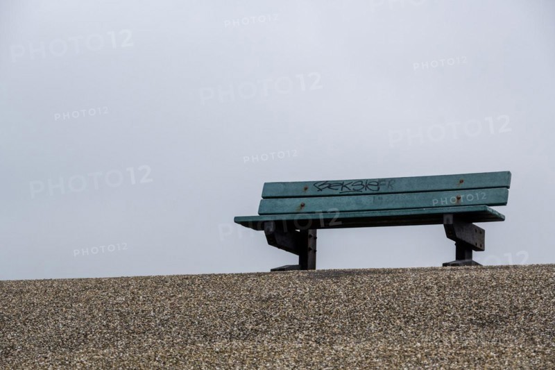 A lonely bench on a pebble beach with a foggy and quiet atmosphere