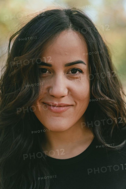 Serene outdoor portrait of a Cheerful hispanic young woman with a slight smile, appearing thoughtful and at peace, selective focus, blurred background with bokeh, daytime, AI generated