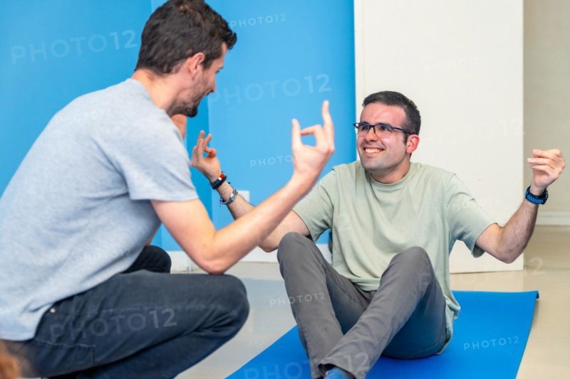 Yoga instructor helping a hand to a disabled man during a yoga pose sitting on the mat in the class