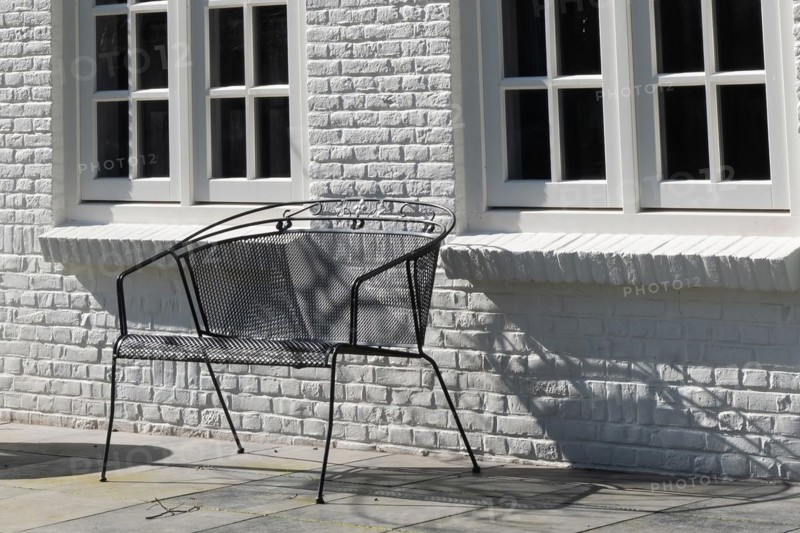 A black metal bench in front of a white wall casts a shadow in the sunlight