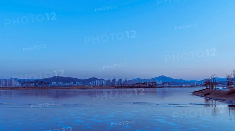 Twilight cityscape with a calm river partially covered in ice, reflecting blue hues, in South Korea
