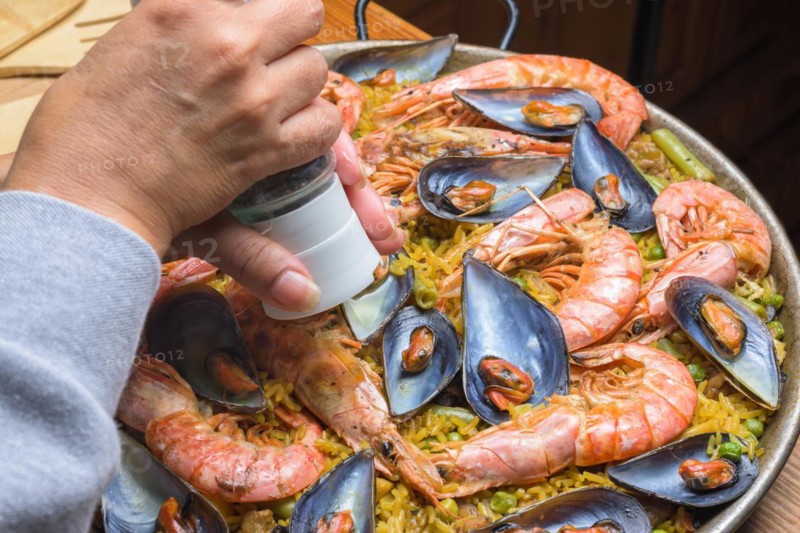 Close-up of a hand seasoning traditional seafood paella with rich colors, typical Spanish cuisine, Majorca, Balearic Islands, Spain, Europe