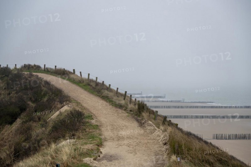 A sandy path through the dunes with a view of the cloudy beach