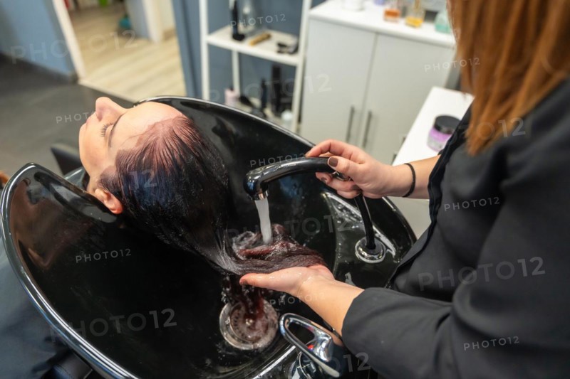 Top view of a female hairdresser rinsing shampoo from a woman's hair at the hair salon
