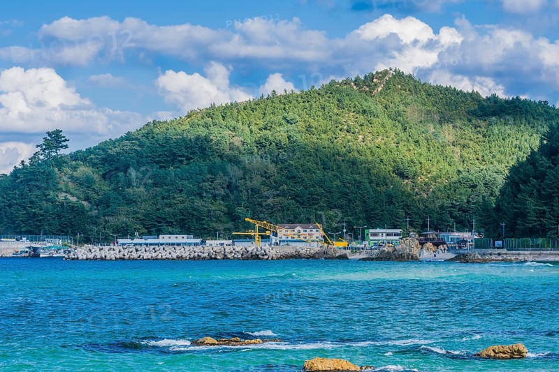 Scenic view of a coastal village by the sea with mountains and blue sky, in South Korea