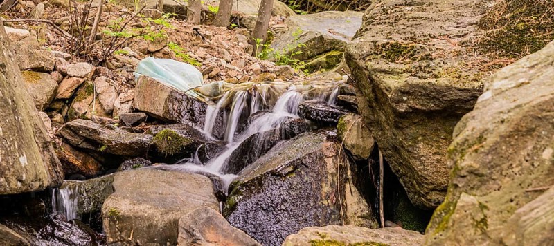 White plastic bag full of trash in stream of water cascading over large rocks and boulders in South Korea