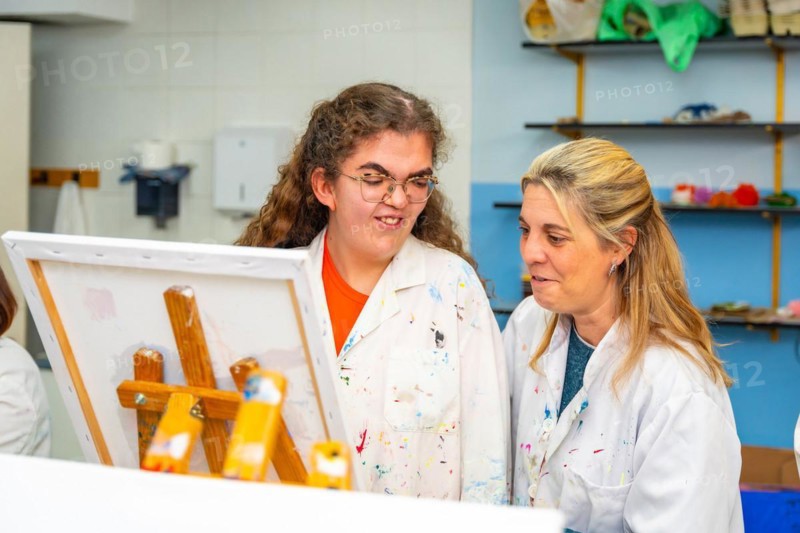 Disabled woman and teacher facing a canvas in a painting class