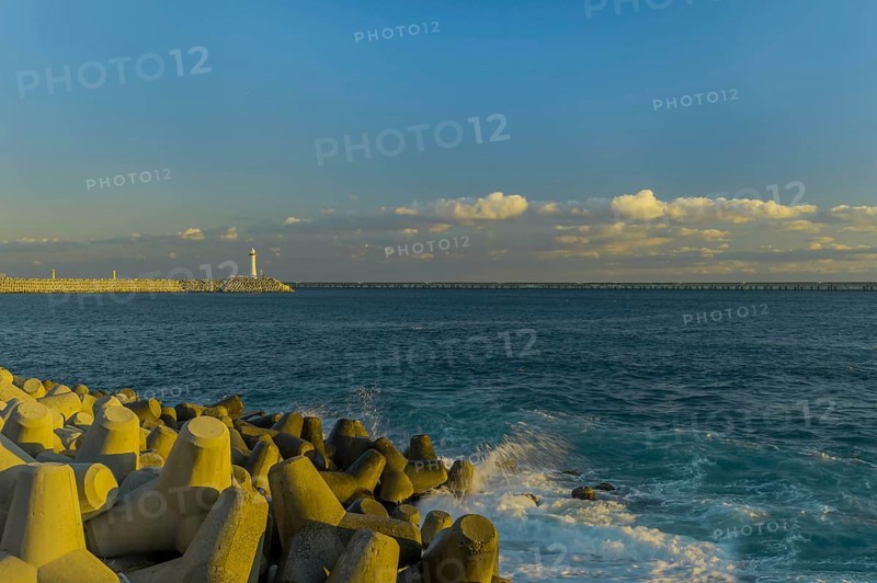Calm seascape of coastline with tetrapods and lighthouse under a dusky blue sky, in South Korea