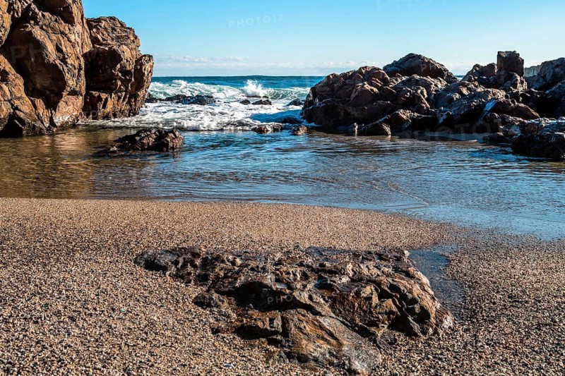 A serene beach scene with waves crashing against large rocks under a clear blue sky, in South Korea