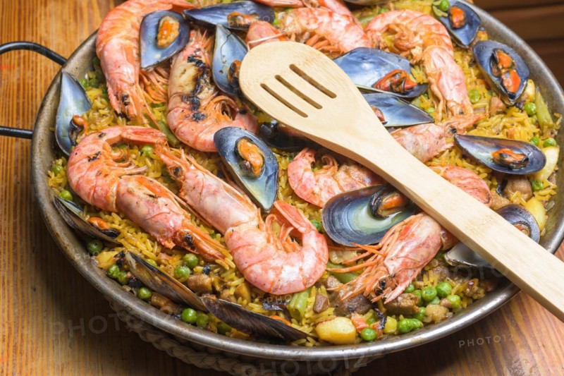 A paella full of seafood, peas, and rice served in a pan with a wooden spoon, typical Spanish cuisine, Majorca, Balearic Islands, Spain, Europe
