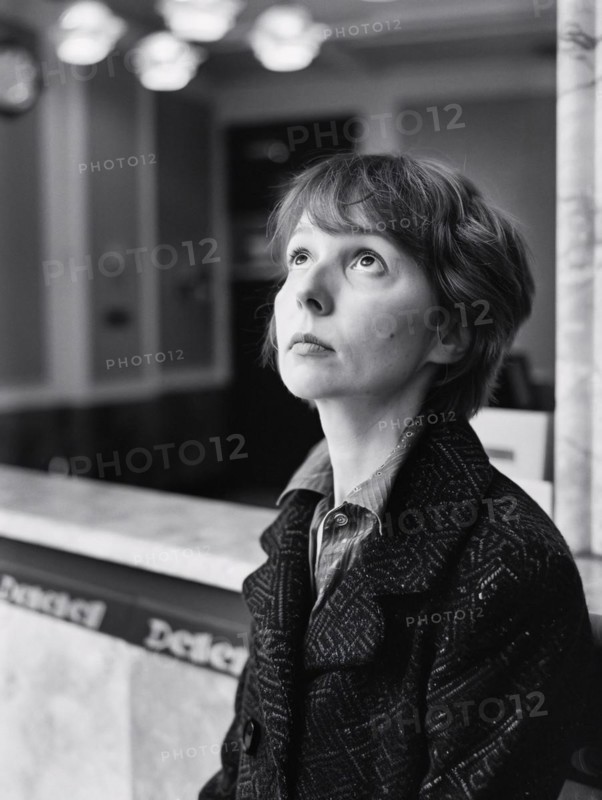 Black and white image of a contemplative woman gazing upwards, standing by a marble counter indoors, AI generated