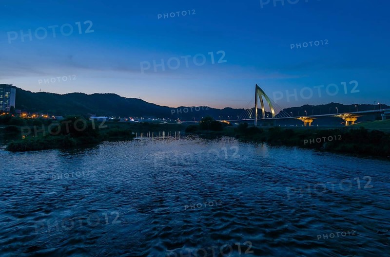 Twilight at a riverfront with bridge and cityscape reflections in blue tones, in South Korea
