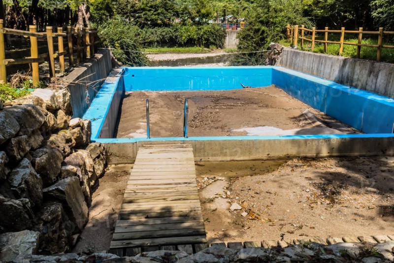 Deserted sandbox surrounded by a blue fence with a small wooden bridge, in South Korea