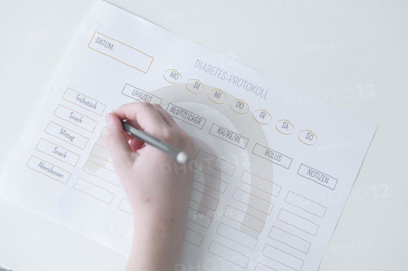 Diabetes log, daily log of food and insulin administration, food log, hand of a child holding a pen and appearing to fill in the log, the paper lies on a white table, Ruhr area, Germany, Europe