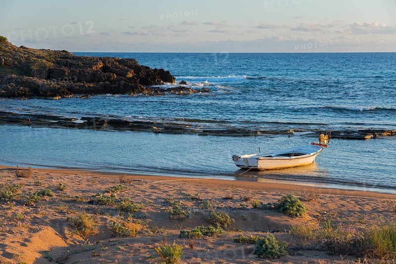 Tranquil scene of a single boat on the coastline with rocks in the soft evening light, Finikounda, Pylos-Nestor, Messinia, Peloponnese, Greece, Europe