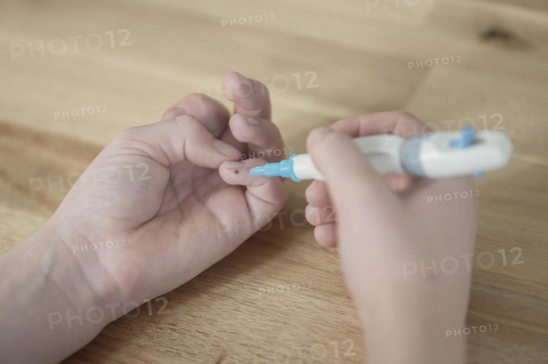 On the left a child's hand with a drop of blood on the little finger, in the right hand the child holds the lancet, lancing device, has just pricked himself, wooden table as background, blood glucose measurement, diabetes treatment, glucose measurement, Ruhr area, Germany, Europe