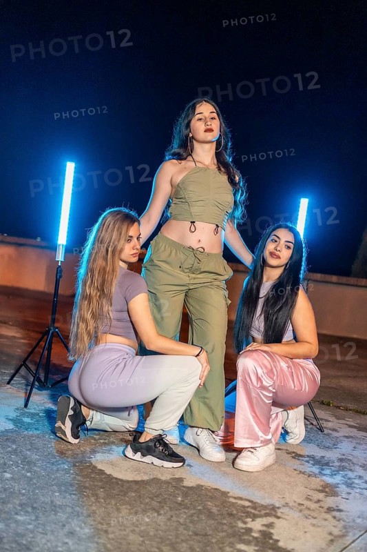 Vertical portrait of three teen trap dancers outdoors at night posing next to neon lights