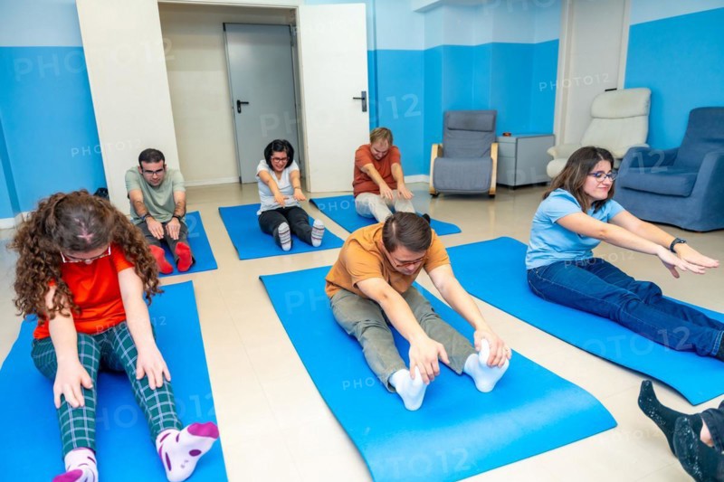 Group of adult intellectual disabled people stretching sitting on a mat during yoga class