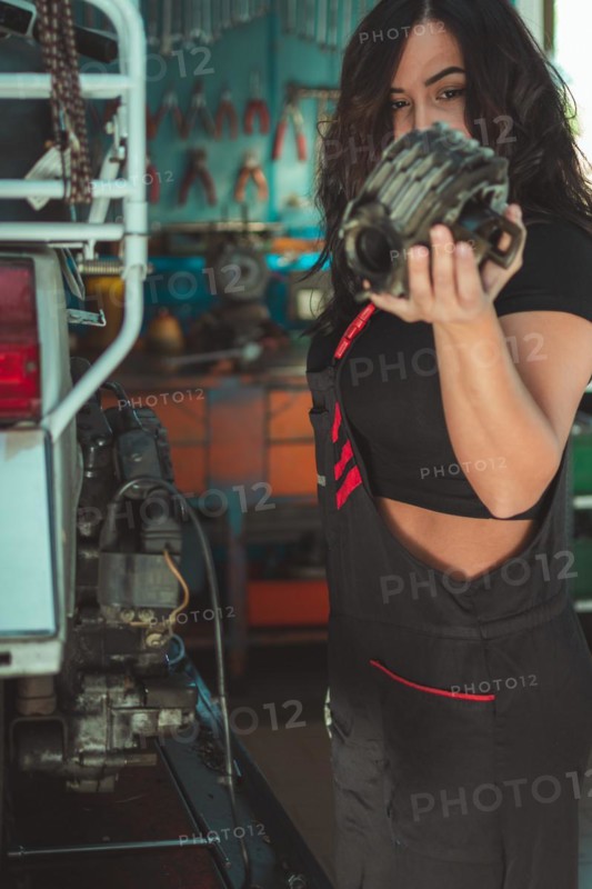 Professional latino female motorbike mechanic holding component of italianvintage scooter in a workshop, a complete tool panel in background with bokeh effect, traditional male jobs by Mixed-race hispanic woman