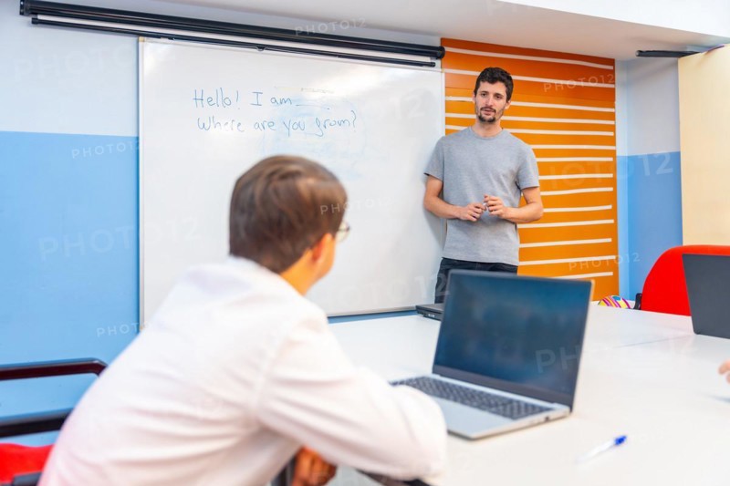 Man with down syndrome using laptop during IT teacher explanation at class