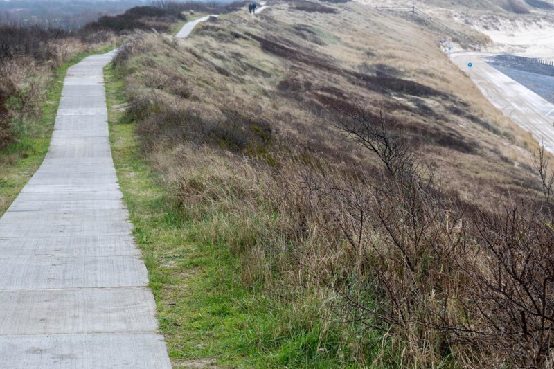 A path winds through the dunes and dry grass under a cloudy sky