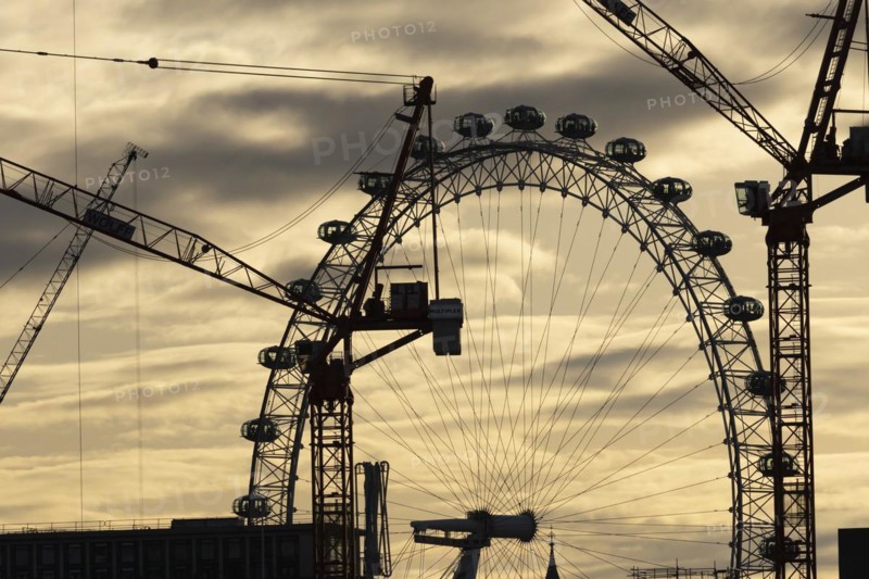 London Eye or Millennium Wheel tourist observation wheel at sunsetwith industrial cranes and cityscape in the foreground, City of London, England, United Kingdom, Europe