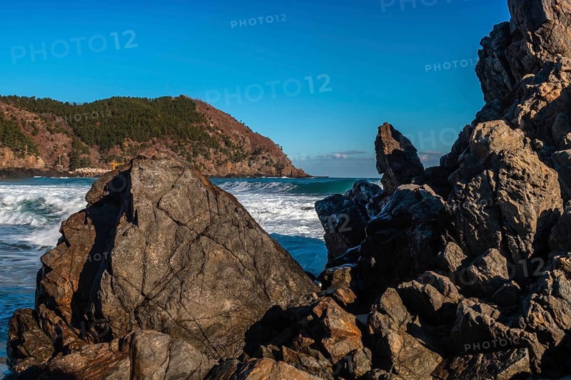 Frothy ocean waves kiss the rocky landscape under the expansive blue skies, in South Korea