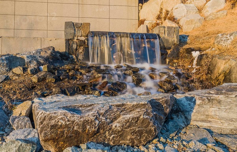 A man-made waterfall flows gently over sunlit rocks, in South Korea