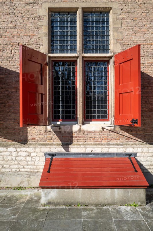 Historic window with red shutters and a matching bench in front of it