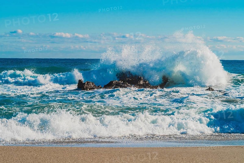 Dynamic white waves collide with coastal rocks on a sunny day with a vibrant blue ocean, in South Korea
