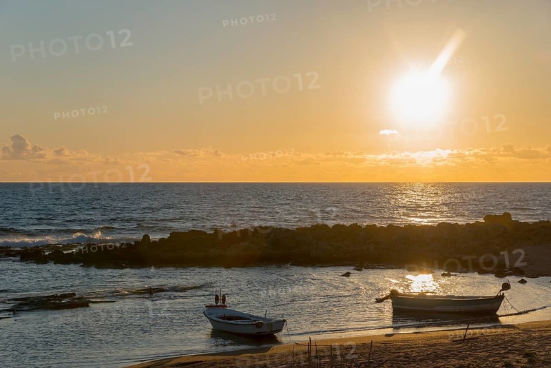 A peaceful sunset by the sea with boats and rocks in the golden light of the evening sun, Finikounda, Pylos-Nestor, Messinia, Peloponnese, Greece, Europe