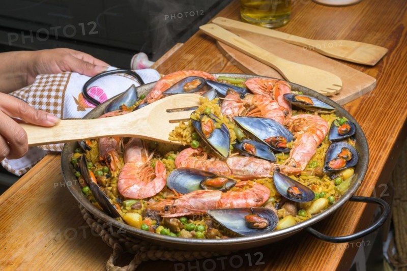A person serving seafood paella with a wooden spatula from a traditional pan, typical Spanish cuisine, Majorca, Balearic Islands, Spain, Europe