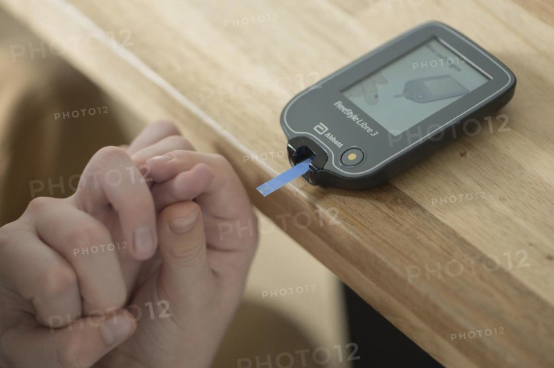 Blood glucose meter with test strips lying on a wooden table, child's hand holding a finger and guiding it to the meter, blood glucose measurement, diabetes treatment, glucose measurement, Ruhr area, Germany, Europe
